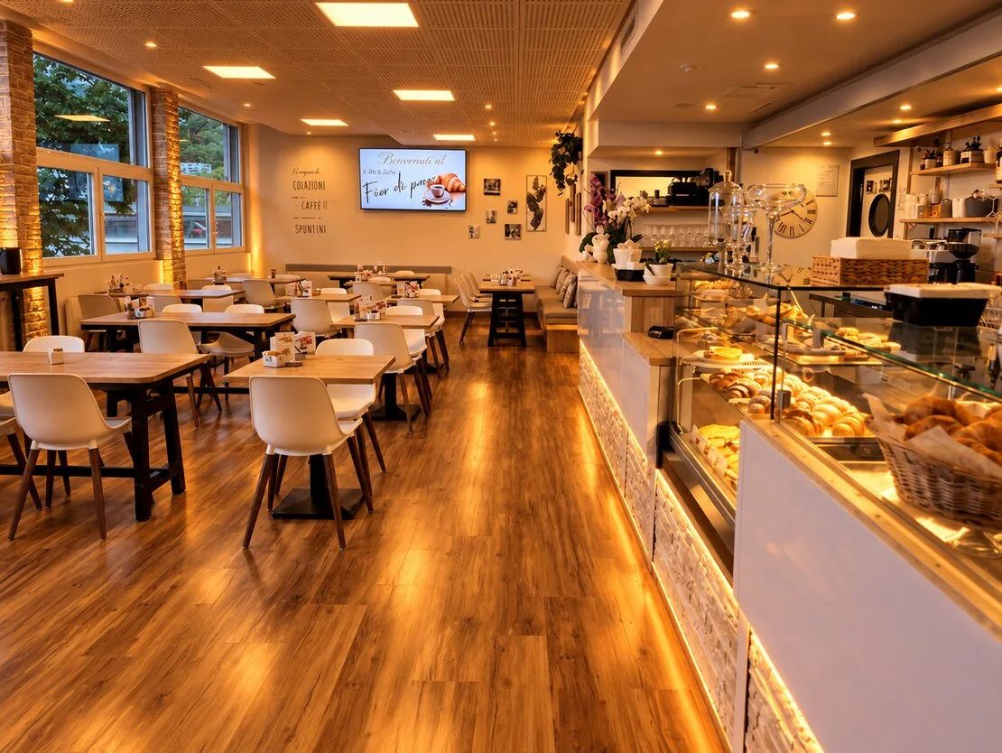 La sala con le luci calde, il pavimento in legno e la vetrina dei dolci lungo il banco